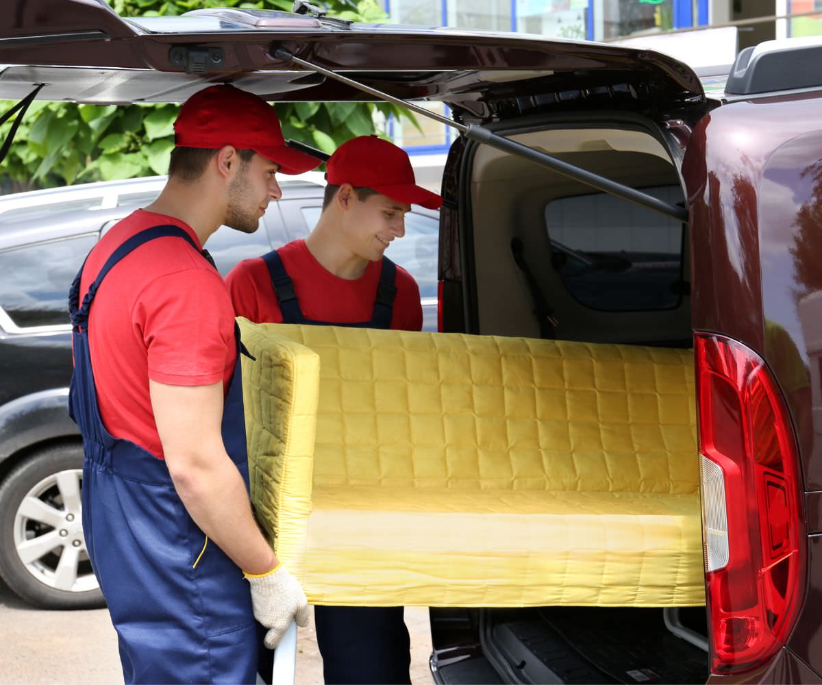 Umzugshelfer laden ein gelbes Sofa in einen Transporter
