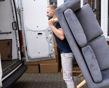 Möbellift Rotenburg: Helfer tragen ein graues Sofa aus einem Transporter